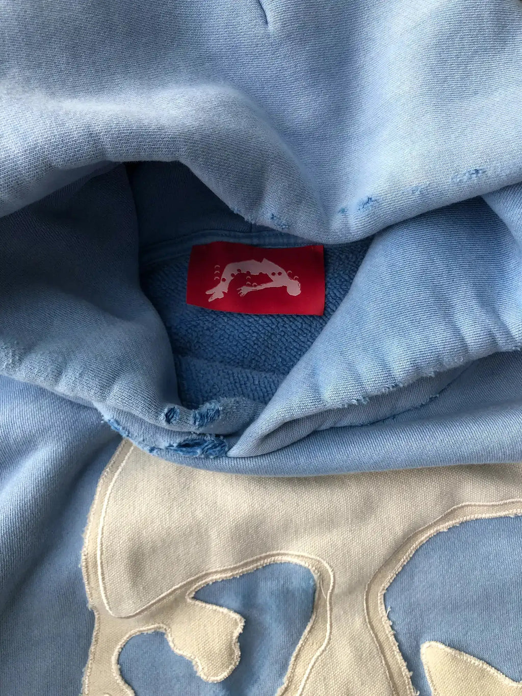 Close-up of red interior tag and raw-cut hood edge on textured fleece-lined hoodie