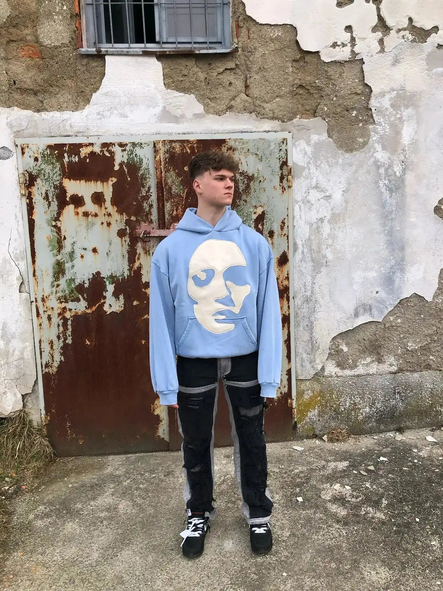 Faceless light blue organic cotton hoodie with dropped shoulders and abstract face appliqué