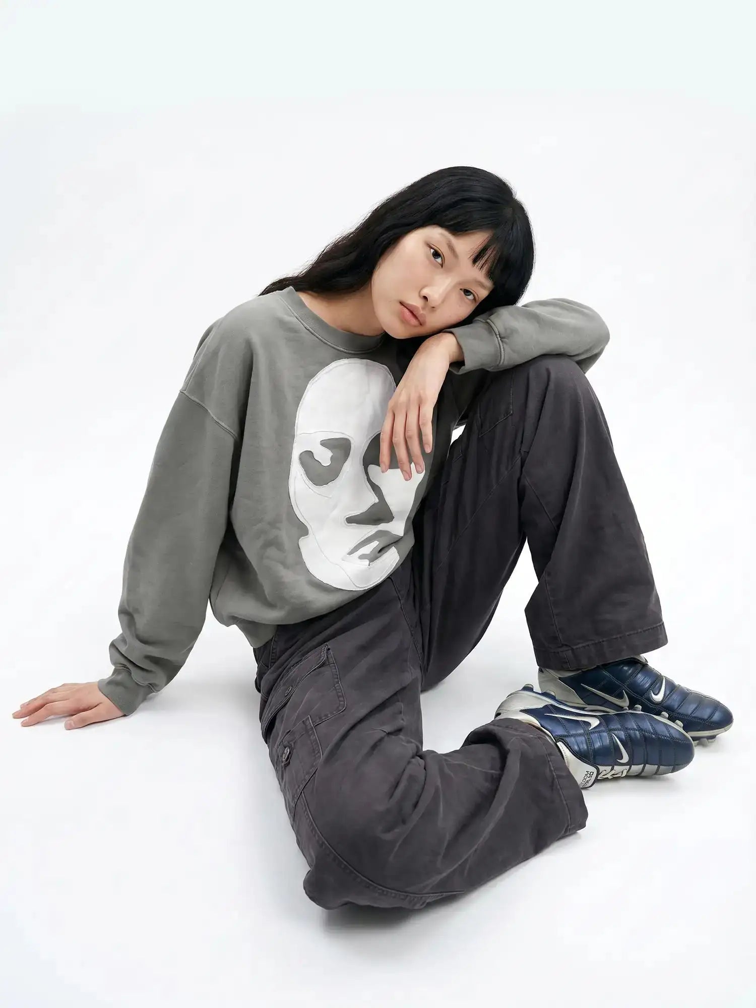 Gray oversized sweatshirt with cut-out eye face appliqué worn by model in wide-leg pants