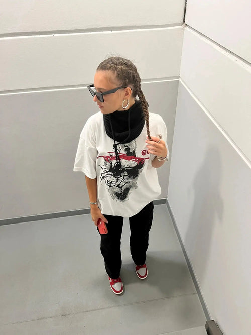 White graphic tee styled with black neck gaiter and red sneakers for Y2K streetwear look