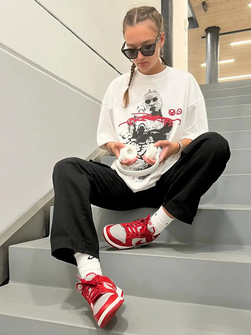 Seated model in white oversized t-shirt with halftone portrait and red accents paired with wide-leg pants