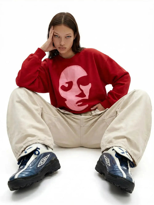 Red oversized sweatshirt with pink face appliqué styled with beige wide-leg pants